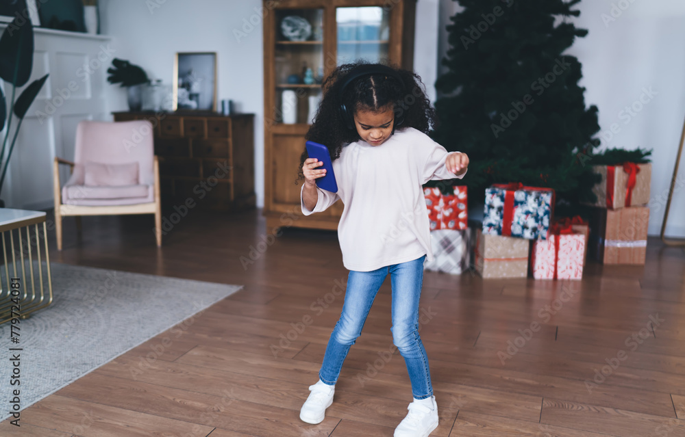 Black girl dancing on floor in living room while holding smartphone