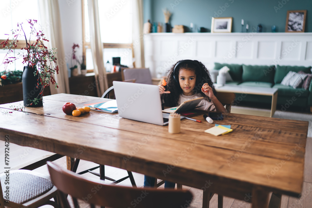 Cheerful black girl using laptop while sitting at wooden table and ...