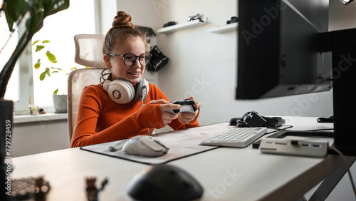 Teenage girl is sitting in a comfortable computer chair, holding a white gamepad in her hands and playing a game on a PC or console. Slow motion shooting.