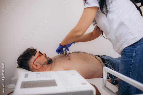 An electrocardiogram procedure for diagnosing heart disease in a hospital ward. The electrocardiograph is seen in the foreground. Concept of ECG or EKG, electrocardiogram in young people.