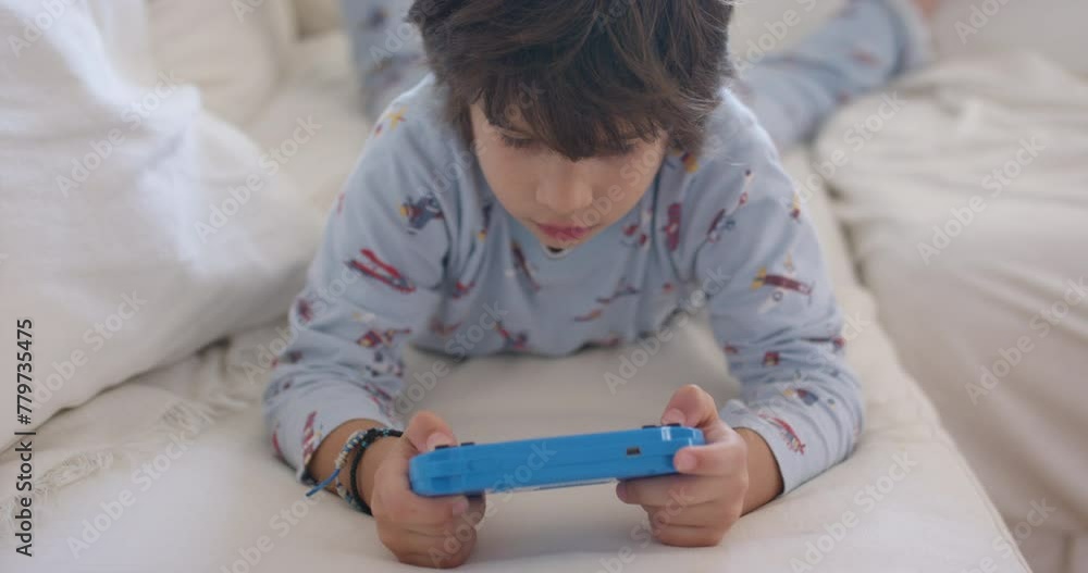 Young boy engrossed in playing a handheld game console on a couch Young boy engrossed in playing a handheld game console on a couch
