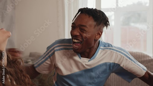 Rival football fans blue fan celebrates in front of red fan on a sofa in slow motion