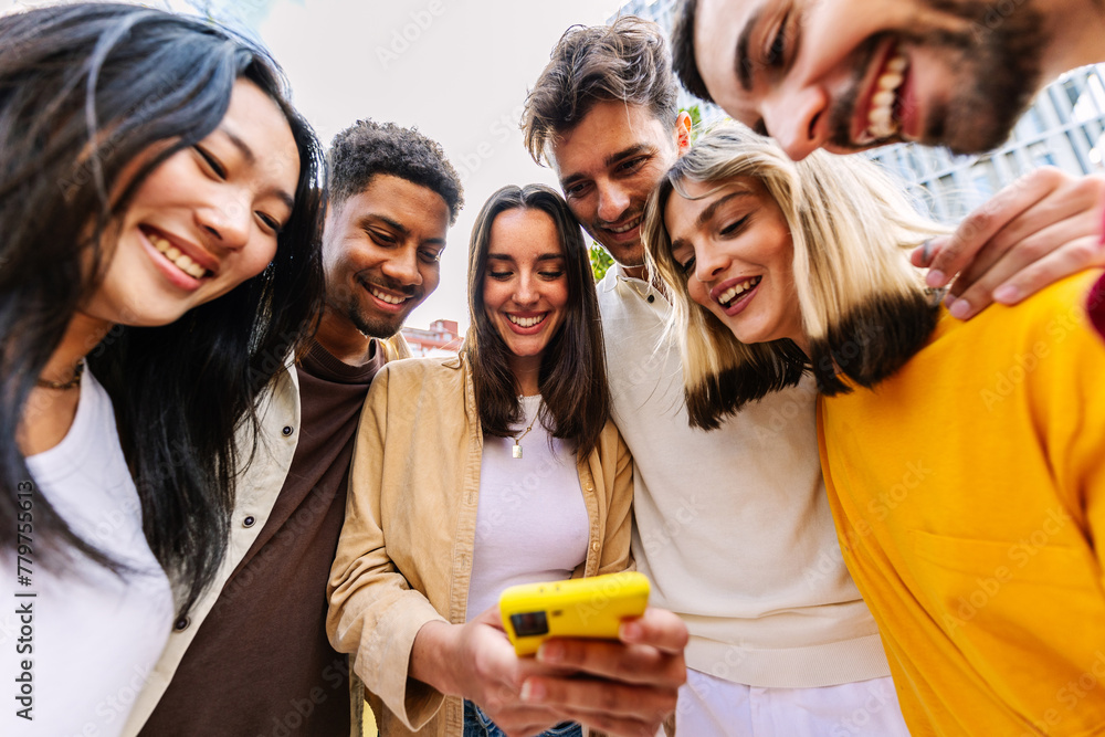 © Xavier Lorenzo - Group of young happy people using mobile phone at city street. Millennial diverse friends enjoying social media content on cellphone app. Technology lifestyle and youth community concept.