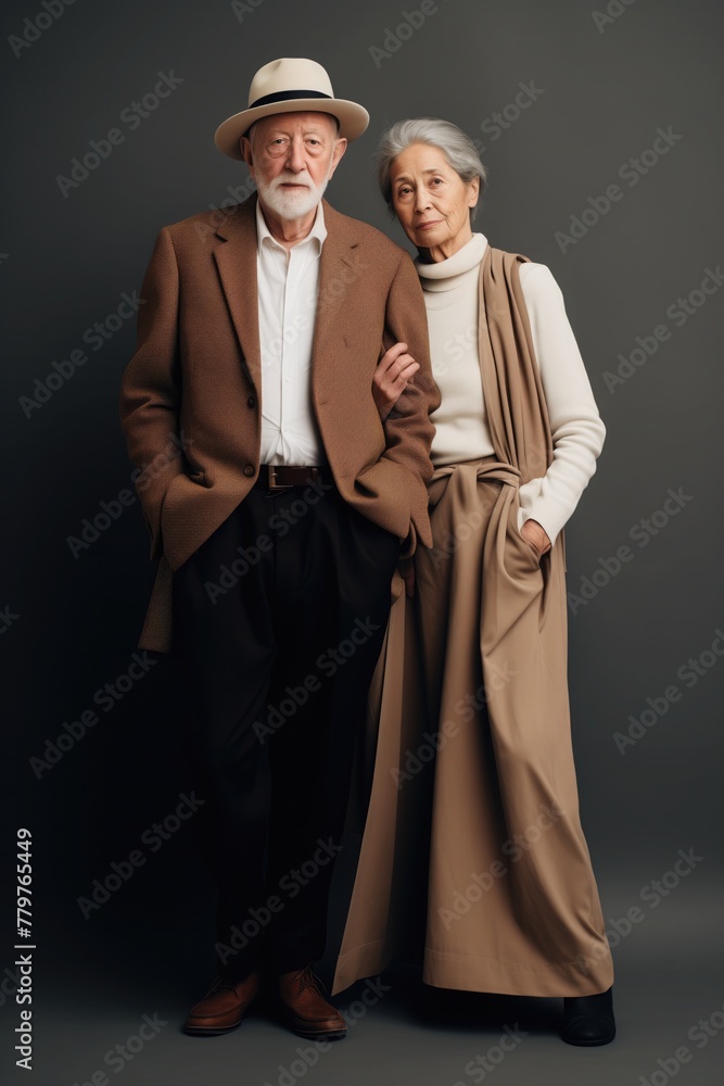 An elderly couple in stylish, elegant minimalist attire, standing against a dark background