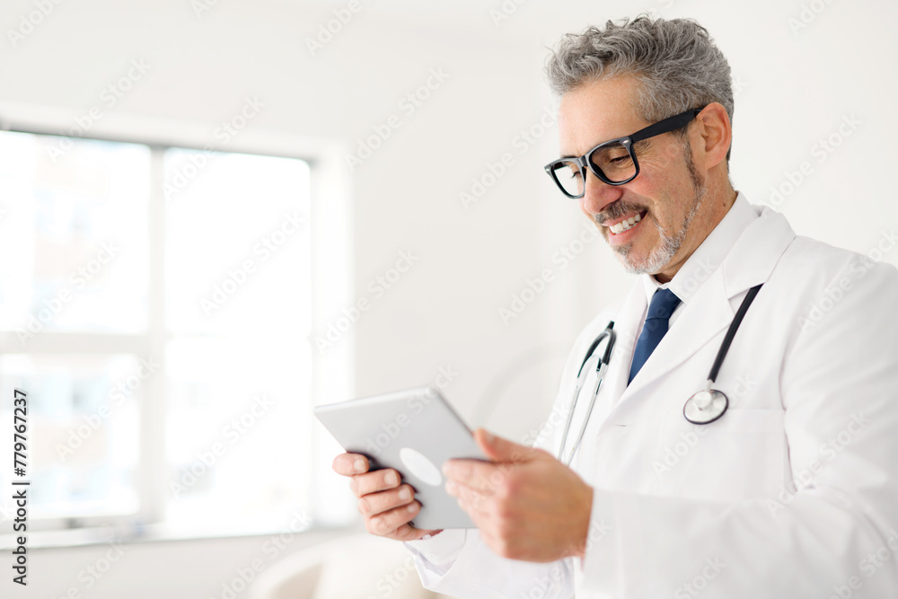 A senior doctor with a gentle smile reviews data on a tablet, a sign of embracing modern medical technology in patient care, side view. Healthcare and technology concept A senior doctor with a gentle smile reviews data on a tablet, a sign of embracing modern medical technology in patient care, side view. Healthcare and technology concept