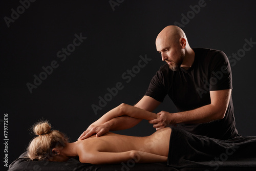 handsome male masseur doing a massage on a girl's hand in a black room, therapeutic relaxing massage concept