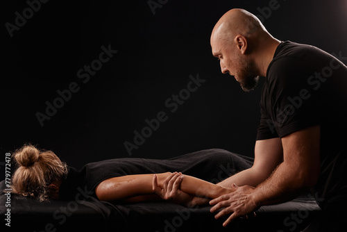 male masseur giving a hand massage to a girl on a dark background, hand massage