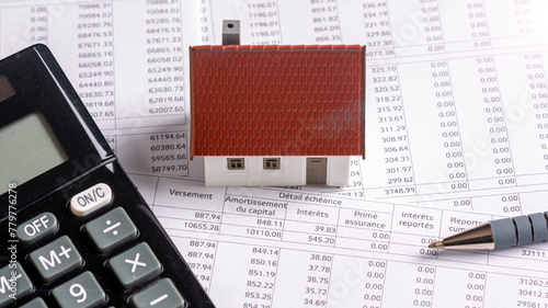Calculette, stylo et maquette de maison individuelle posés sur un document bancaire d'échéancier de prêt immobilier. Concept d'achat immobilier à crédit, de durée et de taux d'intérêt d'emprunt photo