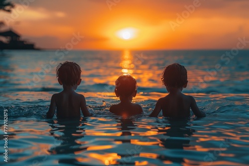 Three children s silhouettes in a sea watching the sun set on the horizon  creating a reflective path