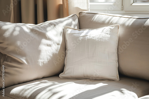 A white square pillow rests on a light gray sofa bathed in warm sunlight.