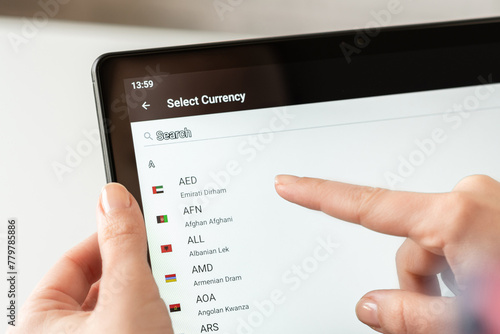 Woman finger of hand choosing foreign CHF, swiss franc currency from the list on the tablet for buying choosing online shopping, booking hotel photo