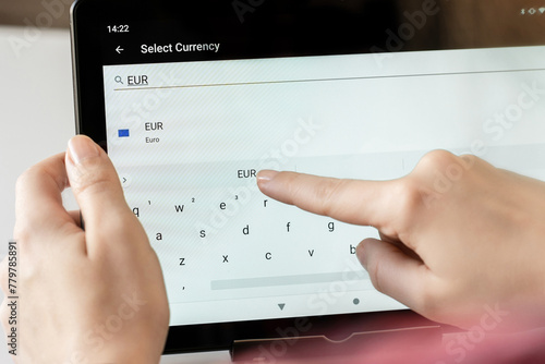 Woman finger of hand choosing foreign eur, euro currency from the list on the tablet for buying choosing online shopping, booking hotel