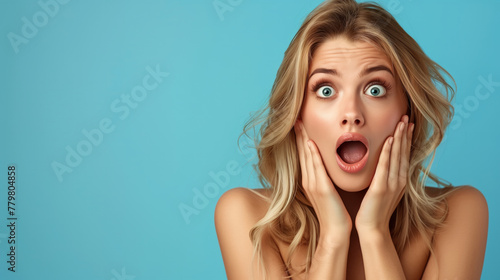 A woman with green eyes and blond hair is making a surprised face. She is wearing a blue shirt. Photo of pretty impressed lady hands touch cheeks open mouth empty space isolated on blue background