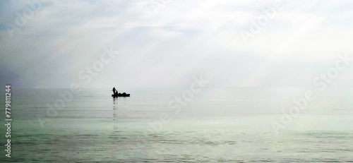 Shot of a man on a small catamaran boat by the horizon, which is hard to detect because of the fog and humidity. Outdoors
