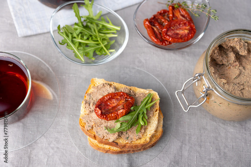 Chicken liver pate with wheat bread, arugula, sun-dried tomatoes and black tea. Homemade traditional rustic cuisine. Breakfast or snack option. Selective focus, close-up.