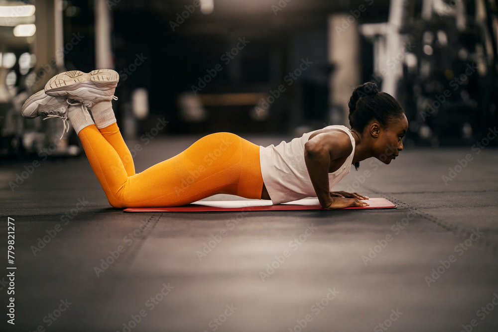 Naklejka premium A muscular black sportswoman in shape practicing pushups at gym.