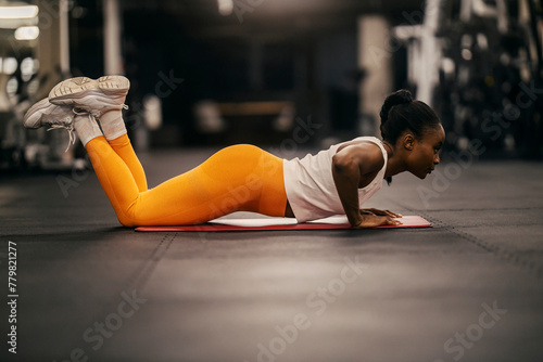 A muscular black sportswoman in shape practicing pushups at gym.