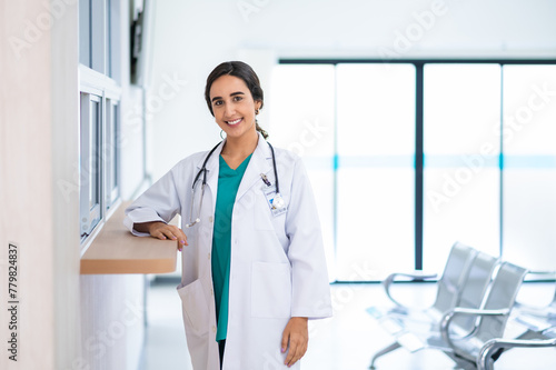 Profile photo of attractive smiling female doctor wearing white medical gown with stethoscope, standing in hospital corridor. Medicine and health care concept with copy space. looking at camera.