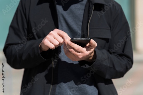 Close-up of the hands of a caucasian young man in casual clothes using a mobile phone while walking outdoors on a warm spring day. Lifestyle, Technology, Work, Freelancing