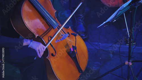 Close-up of a cello, emphasizing its wooden texture and intricate details. The image captures the essence of the instrument. A human hand with a bow guides the strings.