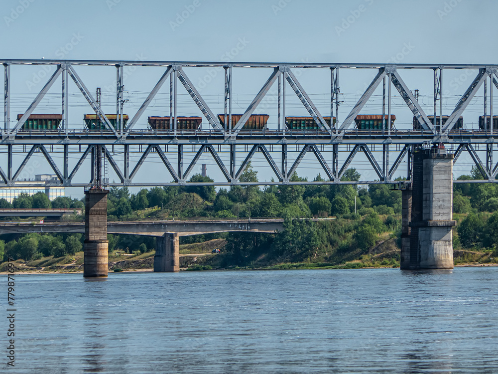 Railway metal bridge over the river. A freight train with wagons for fertilizers is moving along the bridge. Railway metal bridge over the river. A freight train with wagons for fertilizers is moving along the bridge.