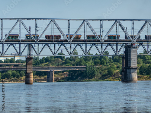 Railway metal bridge over the river. A freight train with wagons for fertilizers is moving along the bridge. © max5128