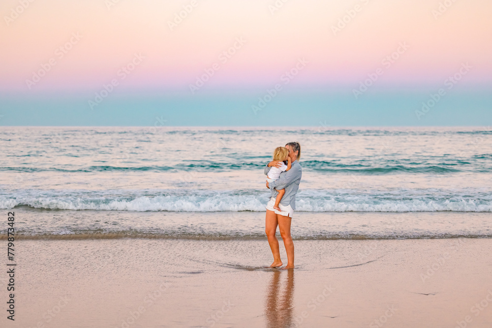Mother carrying son on the beach in pink twilight light. Sunset on the Gold Coast. Mother carrying son on the beach in pink twilight light. Sunset on the Gold Coast.