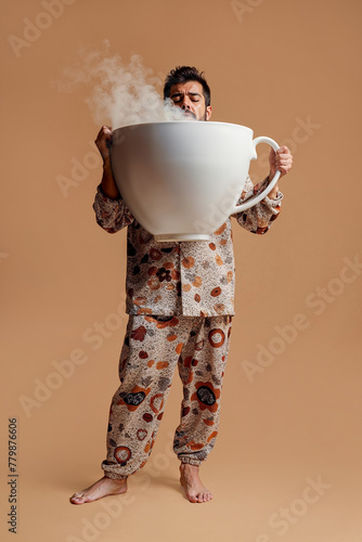 A sleepy man in pajamas drinks a giant cup of coffee to wake up photo