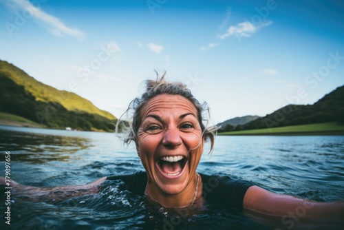 Joyful mature woman swimming in a mountain lake with a selfie perspective © NikoG