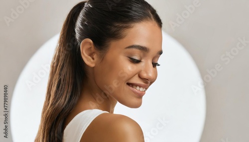 Back view of attractive woman, looking down and smiling, skincare concept. Profile of beautiful female with smooth face skin and natural make-up, straight dark healthy hair 