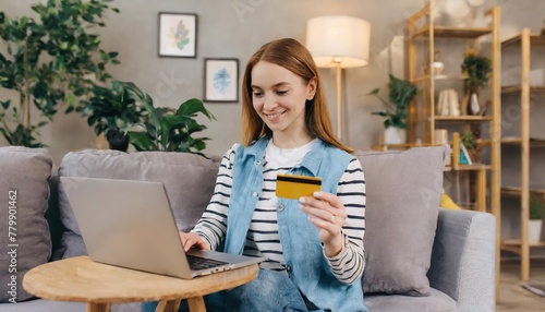  Happy young woman holding credit card and using laptop making payment online. Shopping, e-commerce, internet banking, spending money, working from home concept 