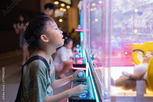 Asian boy at one of the mall stores, playing Claw Game.
