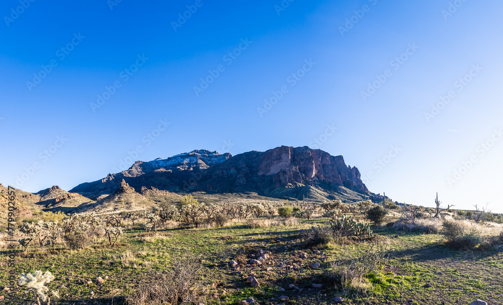 Daytime panorama photo of the Superstition Mountains in Arizona with a light dusting of snow and clear blue sky.