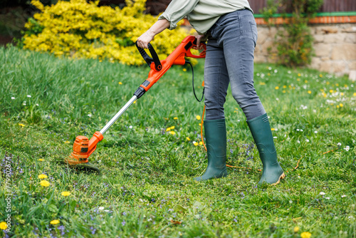 Woman gardener using electric weed trimmer to trim grass in garden. Lawn care in yard © encierro