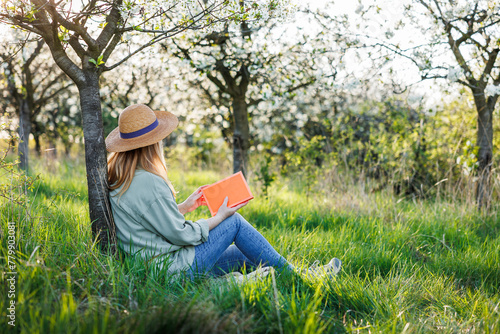 Woman is relaxing in blooming orchard and reading book to improve her mindfulness and mental health. Digital detox outdoors at springtime © encierro