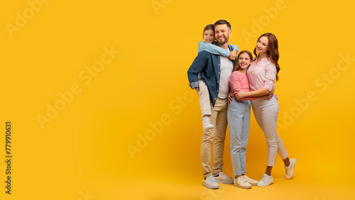 Family embraced and smiling on yellow background