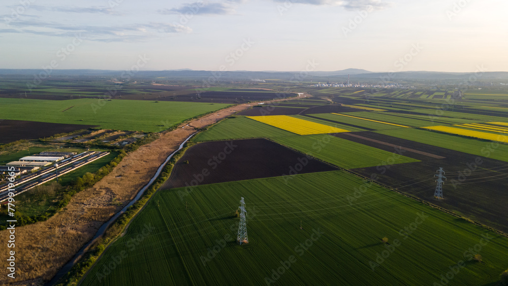 drone view of cultivated fields river, agricultural farm and factory in the distance in early spring at sunset