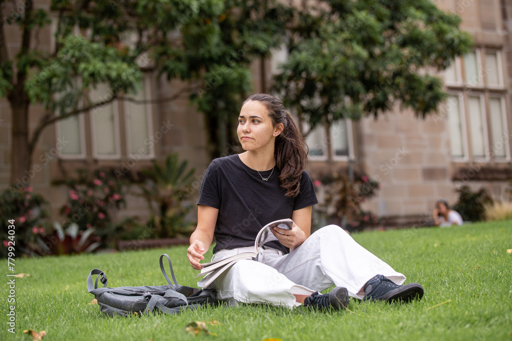 Aboriginal student sitting on the grass with her backpack and books at a university campus Aboriginal student sitting on the grass with her backpack and books at a university campus