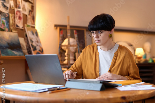 Portrait of female artist using laptop in studio managing creative small business