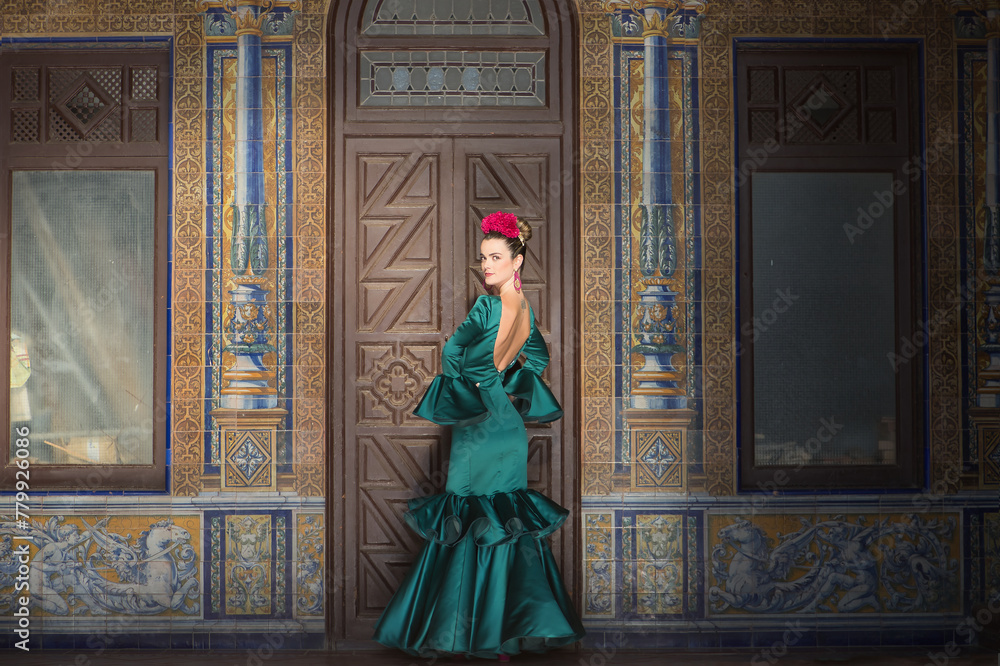 Young, pretty, blonde woman in typical green colored flamenco suit, posing with beautiful tiled wall in background. Flamenco concept, typical Spanish, Seville, Andalusia.