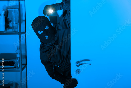 Burglar with flashlight opening a door stealthily