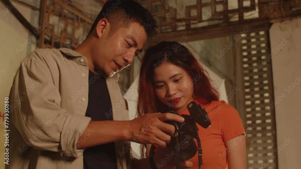 Low angle of young Asian couple checking photos they made on camera inside abandoned building with decorated walls Low angle of young Asian couple checking photos they made on camera inside abandoned building with decorated walls