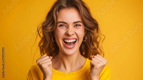 A woman in a yellow sweater is smiling and raising her hands in the air, is has a happy expression on her face. A lady shout loud yeah fist up raise win lottery isolated bright shine color background photo
