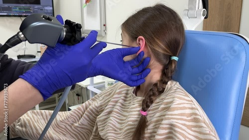 Close-up of otorhinolaryngologist examines preschool girl's ear with otoscope. Adenoiditis as cause of otitis media in children concept. Ear examination photo