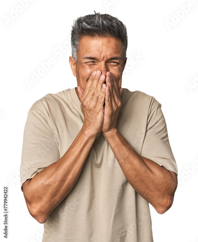 Middle-aged Latino man laughing about something, covering mouth with hands.