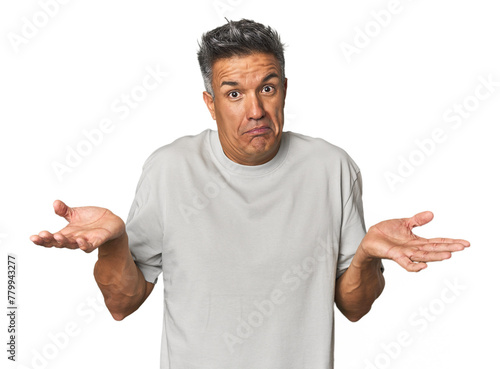 Middle-aged Latino man doubting and shrugging shoulders in questioning gesture.