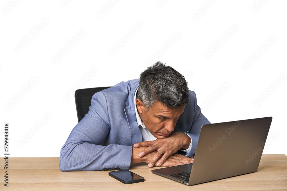 Tired middle-aged Latino man leaning on table while working on laptop Tired middle-aged Latino man leaning on table while working on laptop