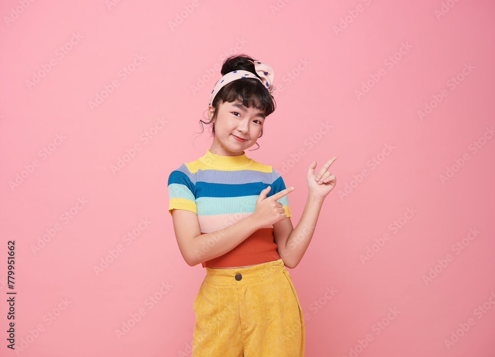 Smiling little asian girl looking and pointing finger shows place for your advertising text Isolated on pink background. Smiling little asian girl looking and pointing finger shows place for your advertising text Isolated on pink background.