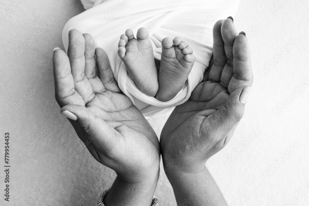 Fototapeta premium The palms of the father, the mother are holding the foot of the newborn baby. Feet of the newborn on the palms of the parents. Studio macro black and white photo of a child's toes, heels and feet.