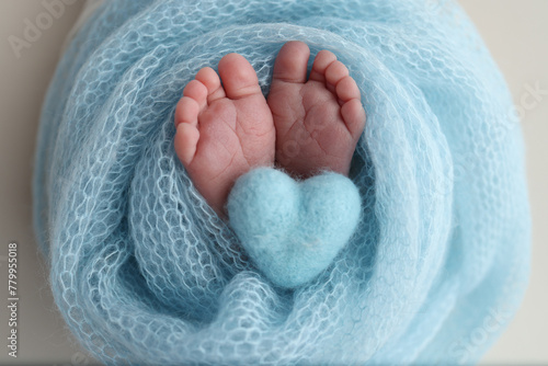 The tiny foot of a newborn baby. Soft feet of a new born in a blue wool blanket. Close up of toes, heels and feet of a newborn. Knitted blue heart in the legs of a baby. Macro photography.  photo
